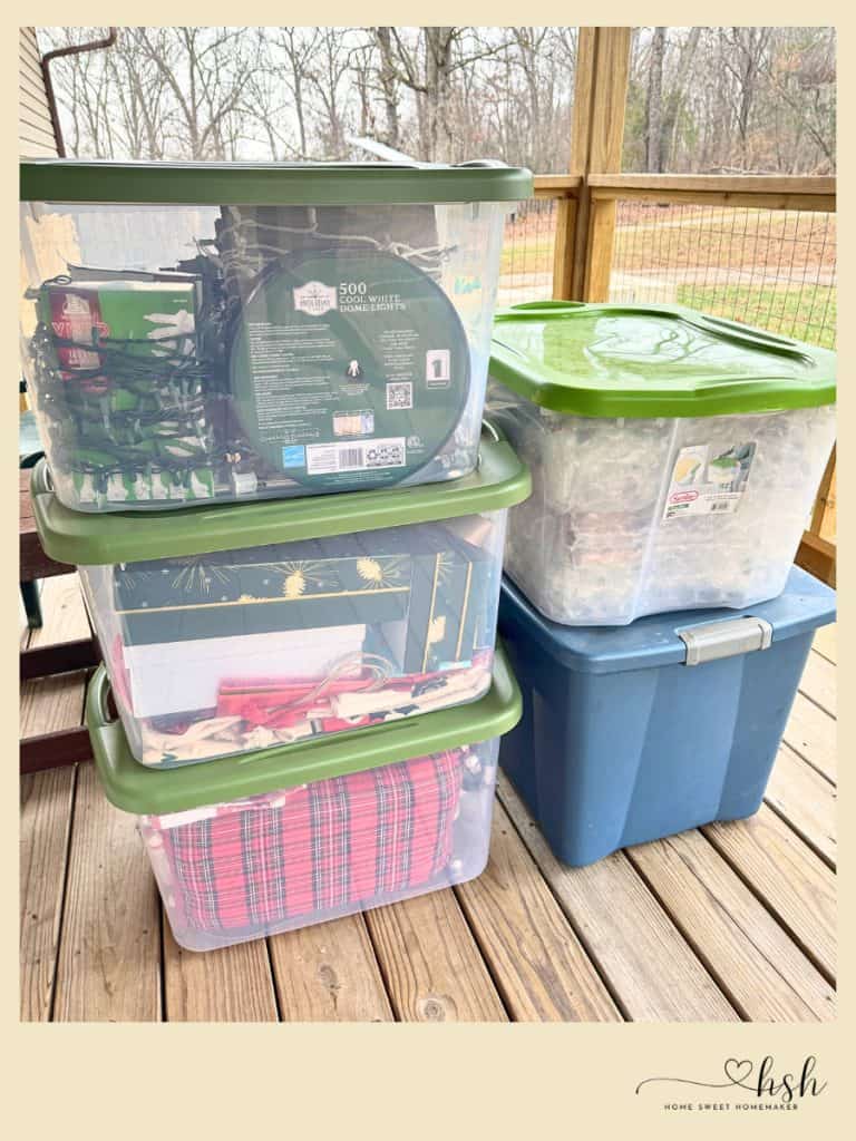 Your Complete Post-Holiday Home Reset Guide 4 Clear plastic storage bins with green lids stacked on a wooden deck, part of an organized post-holiday home reset.