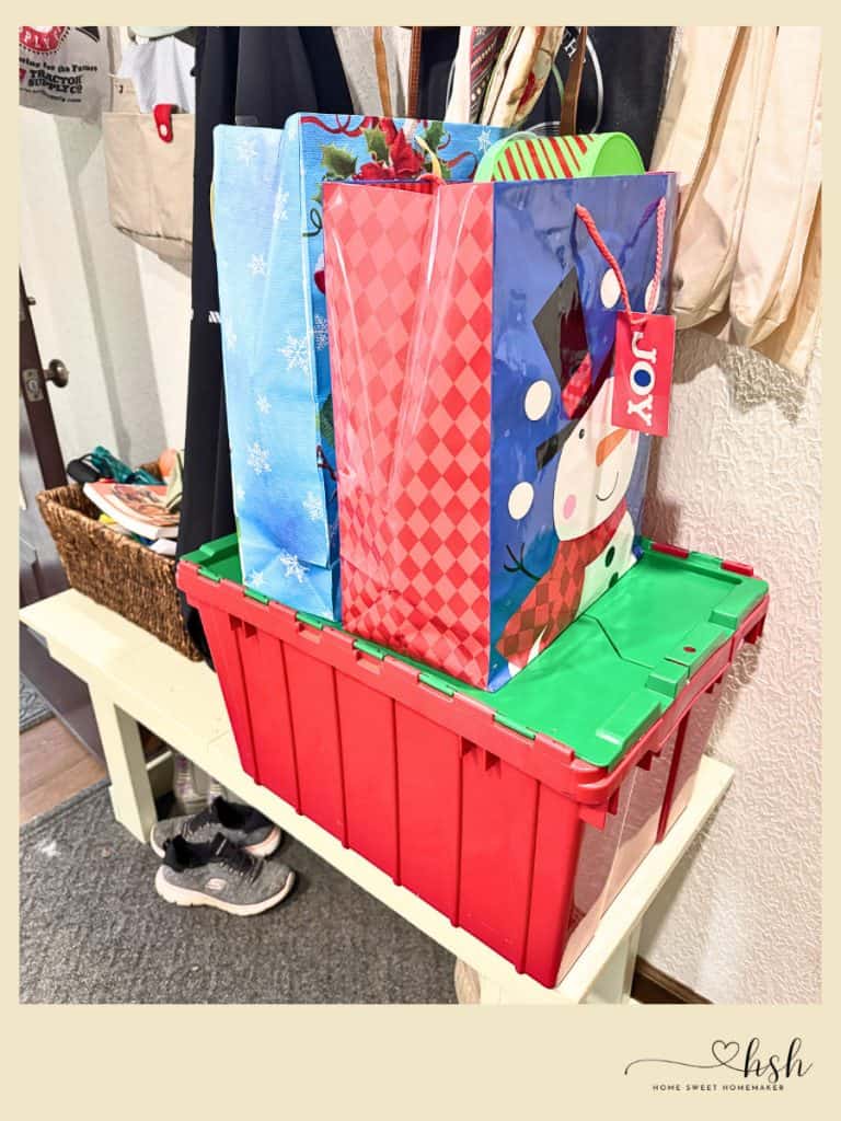 Your Complete Post-Holiday Home Reset Guide 6 Festive gift bags and a red storage container sitting on a white bench during a post-holiday home reset.