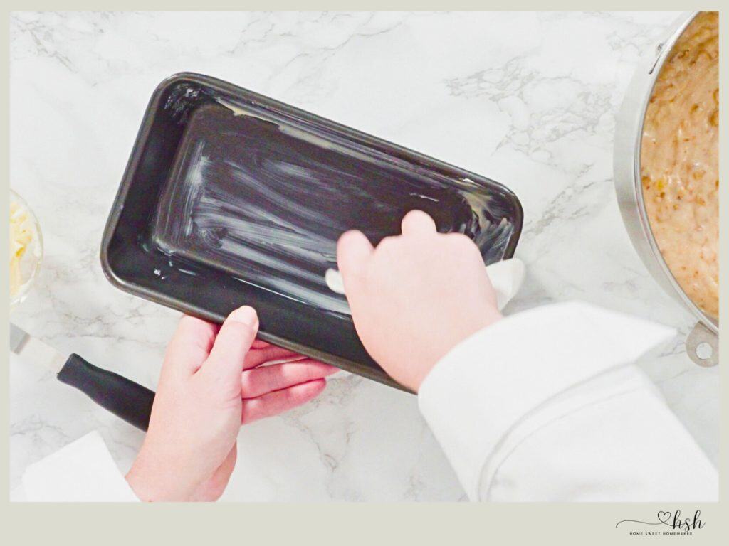Hands greasing dark nonstick loaf pan with butter for pumpkin banana bread baking preparation