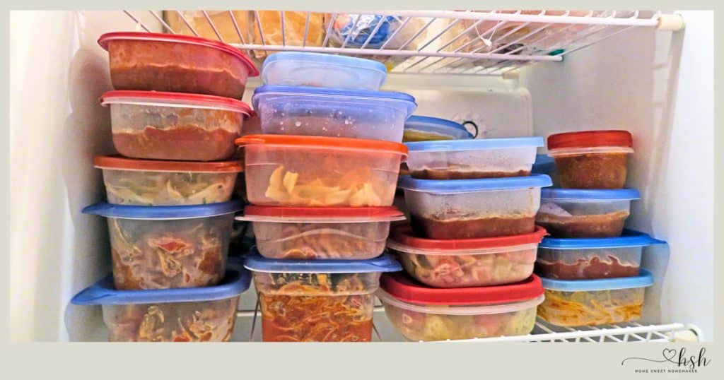 Freezer shelves packed with colorful plastic containers filled with prepared meals and ingredients demonstrating winter freezer meal prep ideas for busy moms.