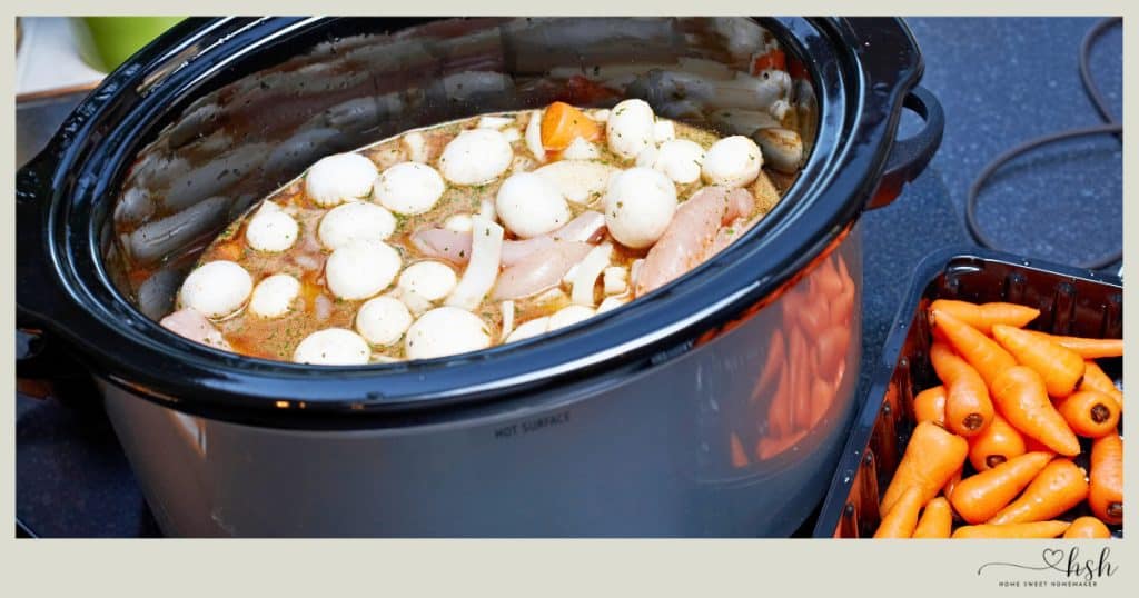 Slow cooker filled with raw chicken breasts, sliced onions, and pearl onions with baby carrots demonstrating easy winter crockpot meal prep for busy moms.